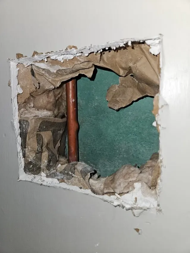 Drywall cut open to reach a leaking copper water pipe in the wall