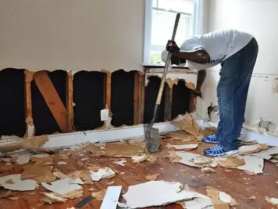 A worker cutting wet drywall off the lower walls of a room after flooding